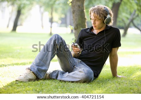 A teenage boy sitting in a park listening to music Royalty-Free Stock Photo #404721154
