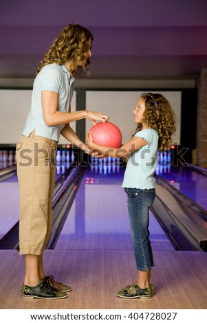 Mother and daughter in a bowling alley, holding a red bowling ball