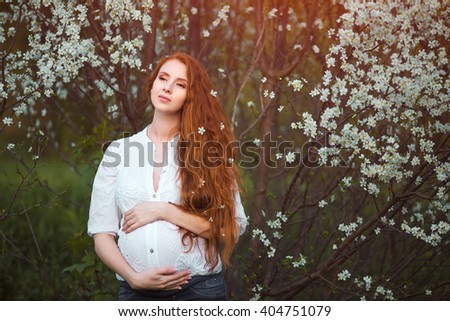 Beautiful pregnant woman standing among trees, outdoor in nature.
