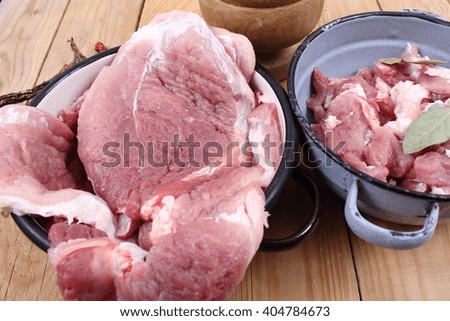 Two metal bowls with sliced raw pork meat and bay leaf on wooden table.