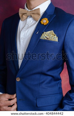 Man in blue suit with brown bow tie, flower brooch, and classic texture pocket square, close up