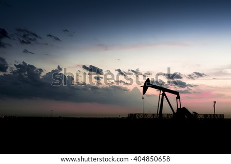 Cloudy sunset and silhouette of crude oil pump unit in oilfield
