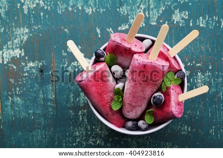 Homemade blueberry ice cream or popsicles decorated green mint leaves on teal rustic table, frozen fruit juice, vintage style, top view