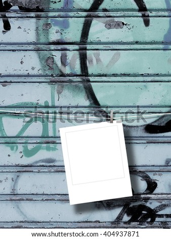 Close-up of one blank square instant photo frame hanged by peg against blue rusty metal shutter background