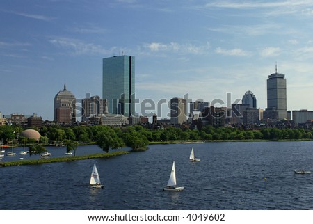 View of the boston skyline from across the charles river, the water is choppy and there are sailboats in the water