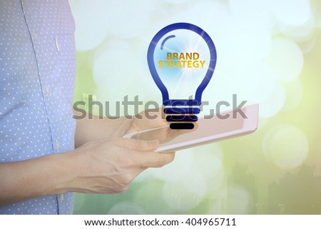 young man holding tablet with BRAND STRATEGY  text on light bulb . soft light with vintage filter. analysis concept 