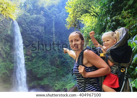 Mother hold baby girl on back in carrying backpack walking in waterfall canyon. Travel adventure and hiking activity with child, active and healthy lifestyle on family summer vacation and weekend tour