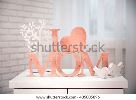 I love mom inscription made of wooden letters with heart on light brick wall and window background