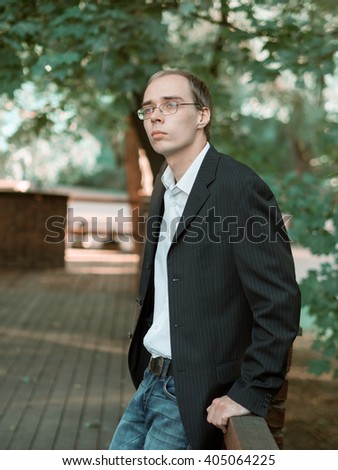 Skinny guy nerd wearing a jacket standing in a park at sunset