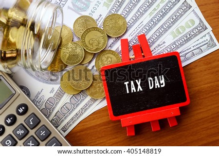 Conceptual image with TAX DAY words. Hundred dollar bills, coins and calculator on wooden background.