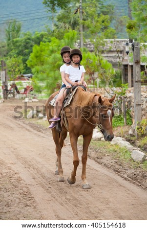 Two asian sisters riding a horse in a small farm