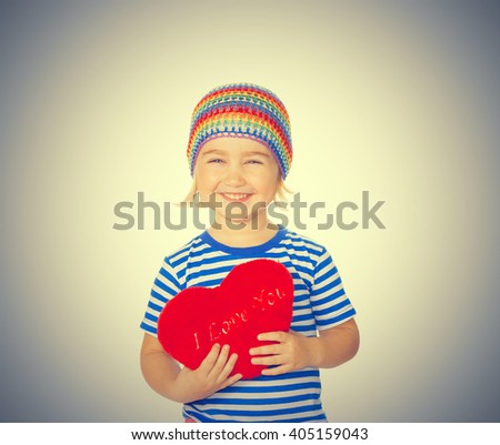 Little girl holding a red heart toy. Isolated on a gray background.