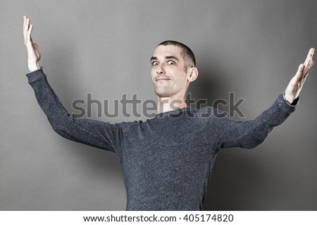 exaggeration concept -  expressive young man with eyes wide open opening his arms wide for theater play or lyric show off, grey background studio Royalty-Free Stock Photo #405174820