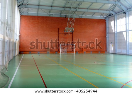 View across in indoor sports court with goalposts and a basketball hoop and net against a red brick wall, empty background view Royalty-Free Stock Photo #405254944