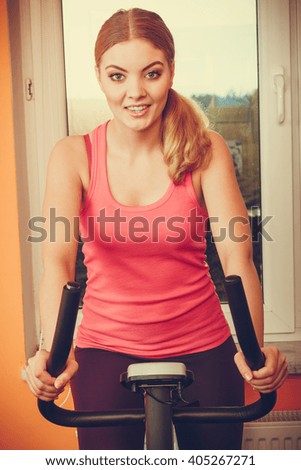 Active young woman working out on exercise bike stationary bicycle. Sporty girl training at home. Fitness and weight loss concept.