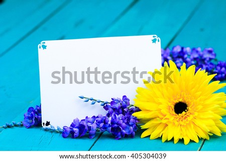 Blank note card with yellow sunflower and purple spring flowers on antique rustic teal blue wood background; springtime or Mothers Day background with white copy space