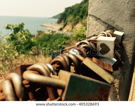Heart padlock amongst rusty padlocks at the fence of a scenic point with seacoast  background