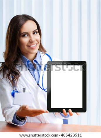 Portrait of happy smiling young female doctor showing no-name tablet pc with blank copyspace area for slogan or text, at office. 