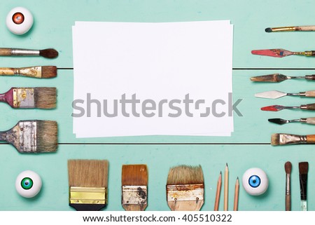 Desk artist with brushes objects. Studio shot on mint wooden background. Top view art workplace. Set grubby brushes. Strange unusual eye. Template for advertising posts on social network