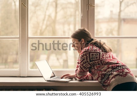 Woman with laptop computer on the window sill. Working at home.