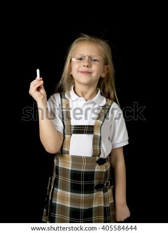 young sweet junior schoolgirl with blonde hair standing happy and smiling isolated in black background holding chalk wearing school uniform in children education success and fun