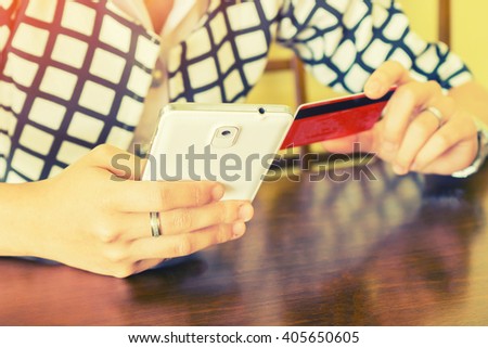 Woman's hand holding smart phone and credit card on a wooden table with working device,coffee morning,business and modern lifestyle concept,hold smartphone  credit card,shopping online,vintage color