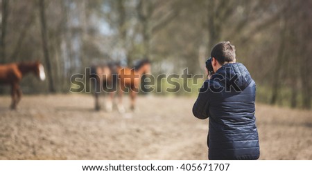 The man takes pictures of horses on the meadow, spring time
