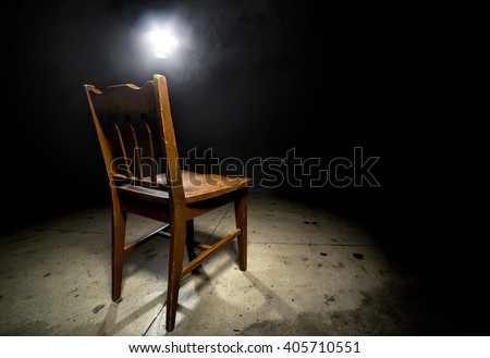 Isolated wooden chair in a dark scary prison with an interrogation spotlight Royalty-Free Stock Photo #405710551