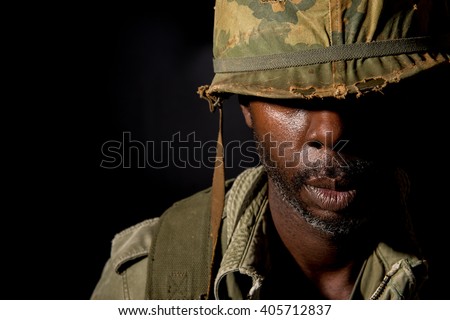 Portrait of a black American G.I.  from the Vietnam War period, with face covered in shadow, against a black background.
