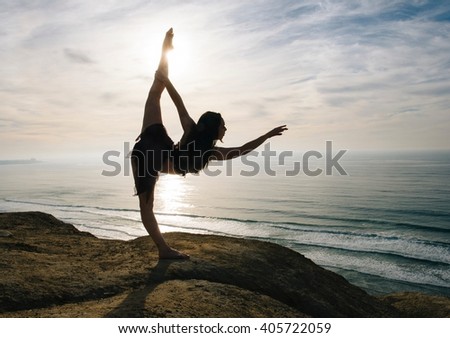 Young female dancer standing on rock, holding leg, stretching in elegant pose, San Diego, California, USA