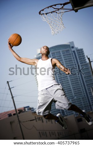 Young African American man jumping with a basketball on an urban basketball court