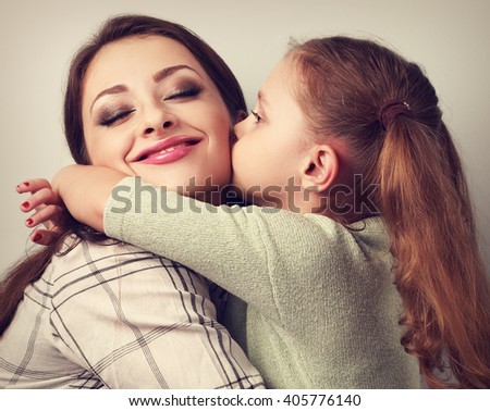 Cute kid girl kissing and cuddling her enjoying beautiful mother in studio. Toned closeup portrait of family love.