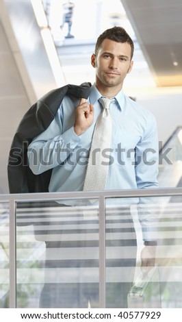 Casual businessman standing in corporate office lobby, holding suitcase.