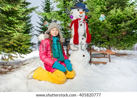 Happy girl with the snowman on a snowy winter walk