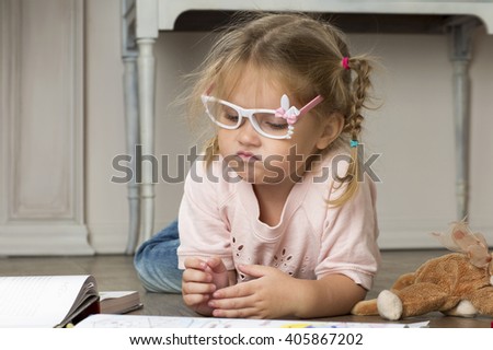 Portrait of a child in glasses with markers. The girl lies on the floor and draws markers.  Royalty-Free Stock Photo #405867202
