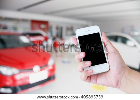hands holding mobile phone with new cars in showroom dealership