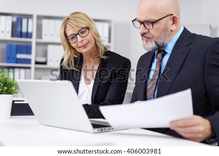 Handsome bald businessman with beard and eyeglasses discussing something at desk in front of computer in office Royalty-Free Stock Photo #406003981