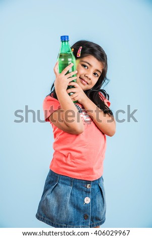 Cute Indian/Asian little girl with a pet bottle of Orange/Mango cold drink or fruit juice, drinking or holding while standing isolated over blue or white background.