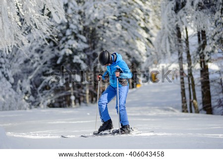 Portrait of young female skier is putting on her skis on a sunny day against beautiful snow covered trees on the background. Ski resort. Carpathian Mountains, Bukovel, Ukraine