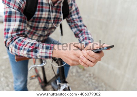 people, travel, technology, leisure and lifestyle - close up of young hipster man in earphones with smartphone and fixed gear bike listening to music on city street