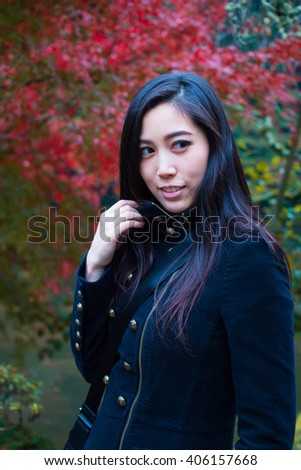Portrait of a young Asian woman with autumn trees on the background. Happy Asian Girl in a park, Woman portrait in a park in Autumn Season