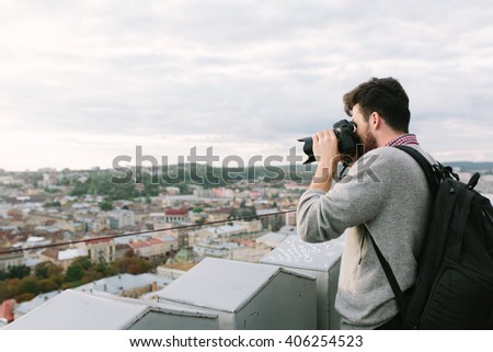 Young man tourist standing on the roof and taking photos of  the city view from above