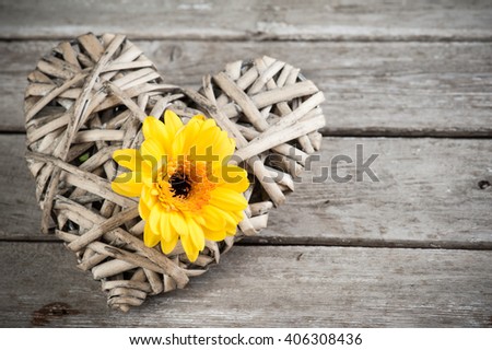 Background with yellow flower and wicker decorative heart on weathered wooden planks. Place for text.