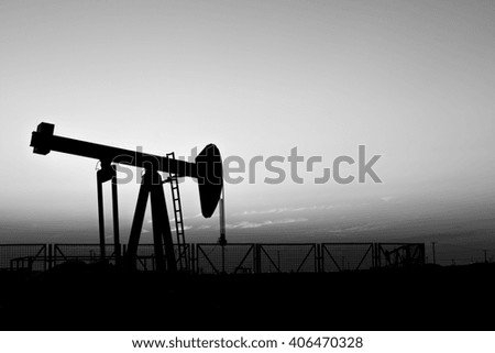 Sunset and silhouette of crude oil pump in oilfield - black and white

