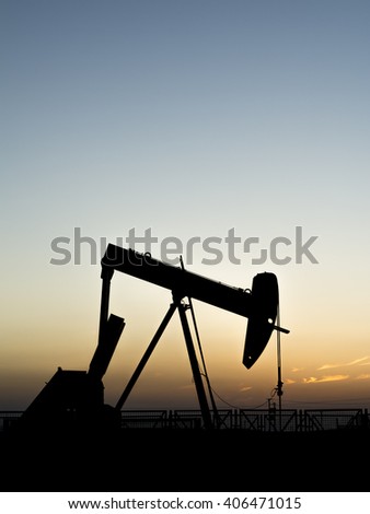 Sunset and silhouette of crude oil pump in oilfield 
