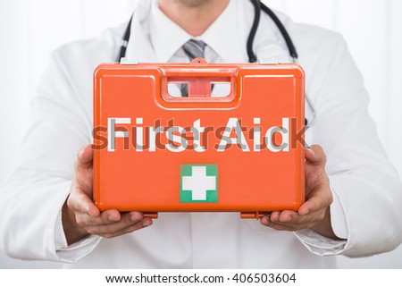Close-up Of Young Male Doctor Hand Holding First Aid Kit Box In Clinic