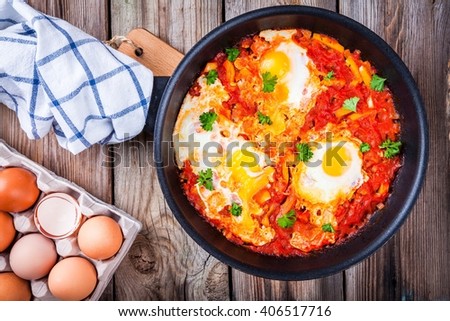 Shakshuka. Fried eggs with tomato, paprika and parsley on wooden table