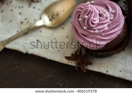 Chocolate cupcakes decorated with purple berries cream and silver sugar balls on brown wooden table