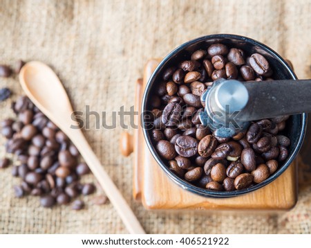 A photo of the roasted coffee beans in a coffee grinder with blur coffee beans , fresh coffee , wooden spoon on sack background.