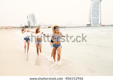Attractive females holding hands and running at beach.